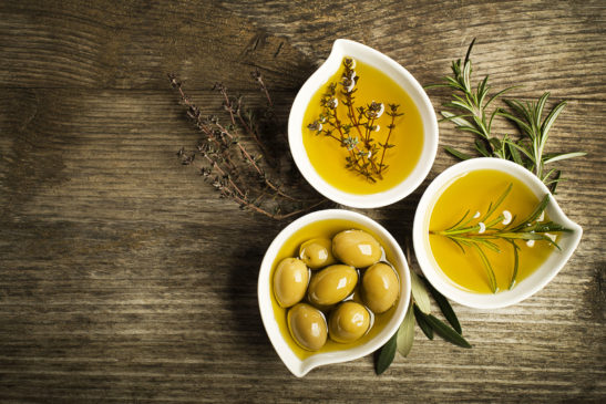 Olivenöl mit frischen Oliven in schönen Schälchen auf Tisch